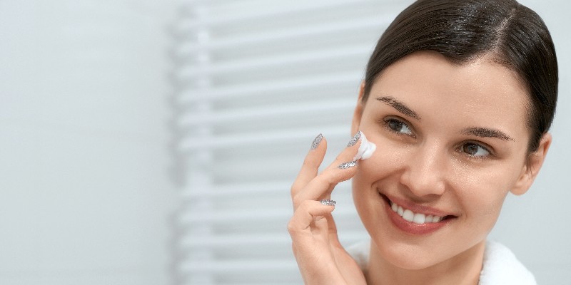 a smiling girl putting moisturizer on her face