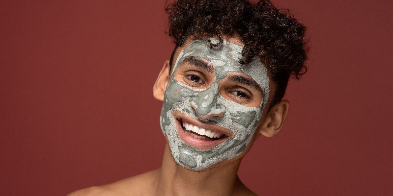 a young boy smiling with clay mask on his face