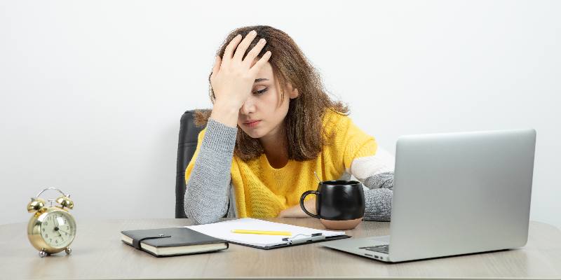 a stressed girl sitting infront of a laptop with hand on her head